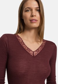 Bordowy top z długim rękawem o prążkowanej strukturze i delikatnym koronkowym dekoltem w kształcie litery V. Miękka tkanina z misternymi detalami koronkowymi wokół kołnierza.