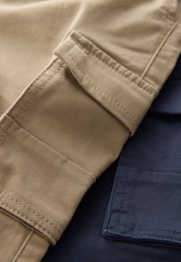 Deux échantillons de tissu : l'un beige avec une texture lisse et des coutures visibles, l'autre bleu foncé avec une surface légèrement texturée et des bords nets.