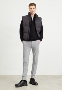 Padded black vest over a black sweater, paired with light gray tailored pants and black chunky shoes. Minimalist design and neutral colors.