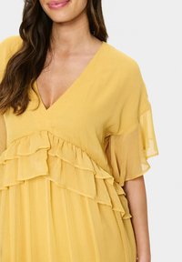 Yellow dress with a V-neck, short flutter sleeves, and layered ruffles across the bust and skirt. Light, textured fabric.