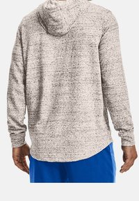 Mężczyzna w jasnoszarym, prążkowanym hoodie i jaskrawo niebieskich spodniach, widoczny od tyłu z rękami swobodnie po bokach.