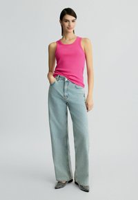 Enganliegendes pinkes Ripp Top, hochtaillierte, hellblaue weit geschnittene Jeans und schwarz-weiße gemusterte High Heels. Schlichtes Design, lässiger Look.