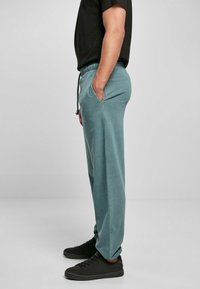 Teal joggebukser med elastisk midje, sidesk pockets og innsnevret bendesign, kombinert med svarte sneakers. Glatt stoff tekstur.