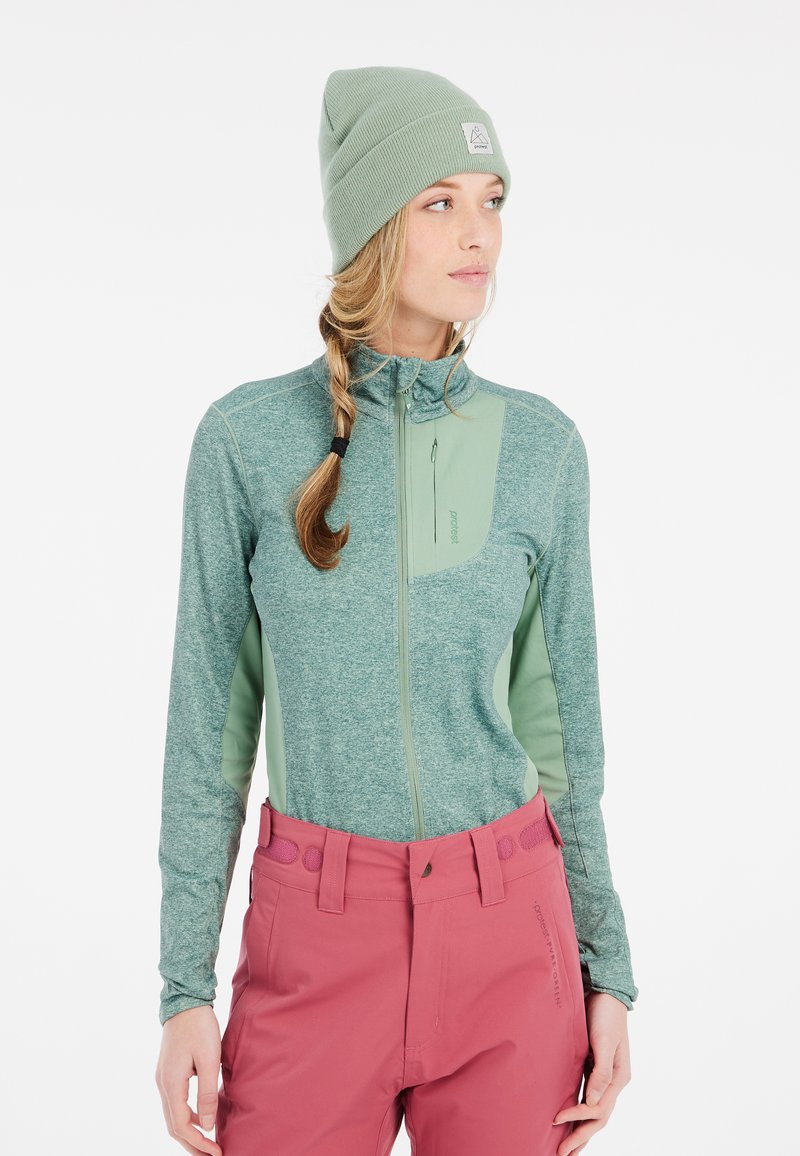 Maglione verde con zip e maniche lunghe, dalla finitura testurizzata e un pannello sul petto di un verde contrastante, abbinato a pantaloni rosa con dettagli circolari.