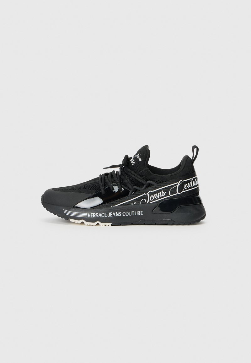 Black athletic shoe with mesh upper and rubber sole. Features branded accents and a sleek design. Reflective details along the sides.