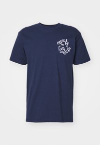 T-shirt de algodão azul-marinho com mangas curtas, apresentando uma estampa branca de uma pomba e o texto "PAZ & AMOR PARA TODOS" no lado esquerdo do peito.