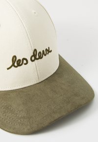 Cream baseball cap with a green suede visor, featuring embroidered text "les deux" in olive green. Structured design with stitching details.
