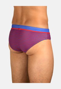 Slip de bain avec des rayures horizontales rouges et bleues, doté d'une ceinture unie bleue. Fabriqué en matériau doux et extensible.