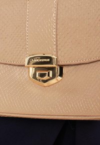 Beige handtas met een textuur en een slangenhuidpatroon, voorzien van een gouden sluiting en een gegraveerd merklogo aan de voorkant.