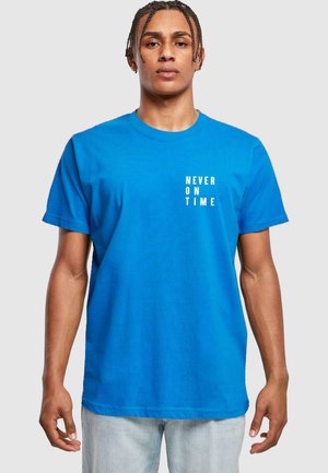 Lys blå bomulds T-shirt med hvid tekst "ALDRIG TIL TIDEN" i en vertikal opsætning på venstre bryst. Korte ærmer, rund halsudskæring.