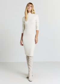 Gestricktes Midikleid in hellem Creme, mit hohem Ausschnitt und langen Ärmeln. Kombiniert mit kniehohen, hellbeigen Stiefeln mit Absatz. Glatte Textur.