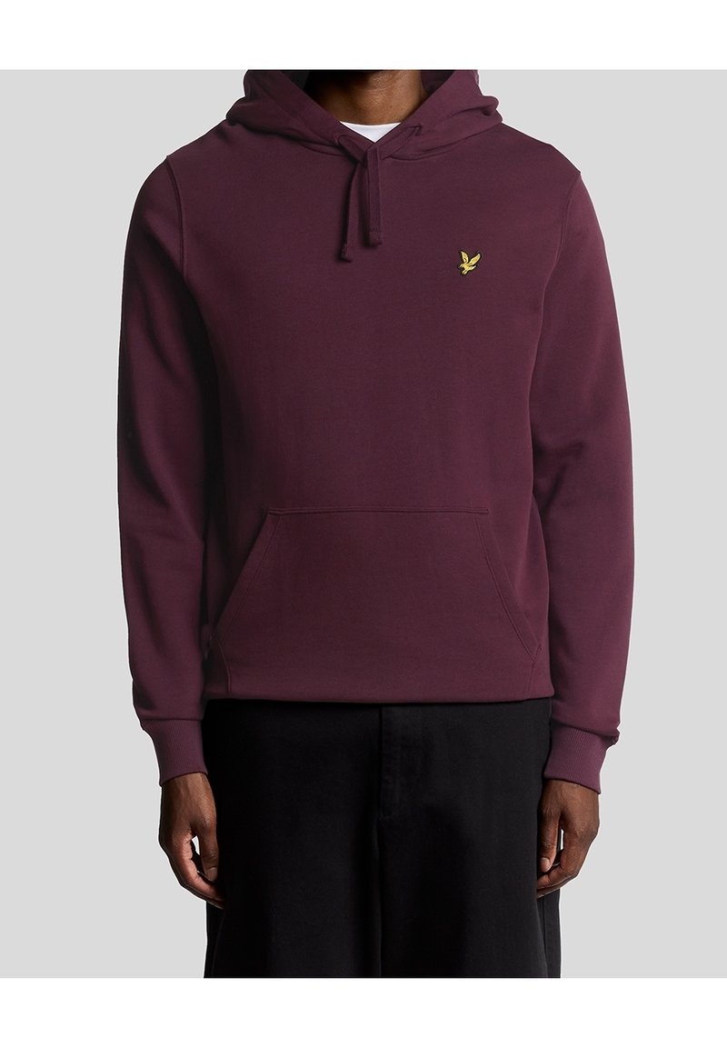Homme portant un sweat à capuche violet foncé avec une poche kangourou et un petit logo d’oiseau jaune sur le côté gauche de la poitrine.