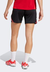 Black athletic shorts with red side accents, paired with white socks and red cleats. Smooth fabric with a relaxed fit, designed for sports.