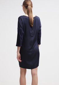 Abito in satin blu navy con maniche a tre quarti, scollatura a V e zip centrale sul retro. Texture liscia, design all'altezza del ginocchio.