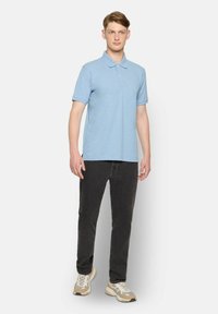 Hellblaues Polo-Shirt mit kurzen Ärmeln, klassischem Kragen und Slim Fit, kombiniert mit schwarzen Jeans und beigen Sportschuhen.