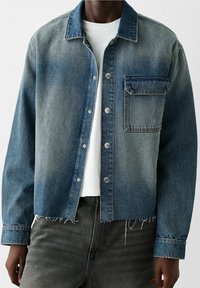 Giacca di jeans in gradiente blu con chiusura a bottone, tasca sul petto e vestibilità ampia. Presenta orlo sfrangiato e maniche a taglio dritto.