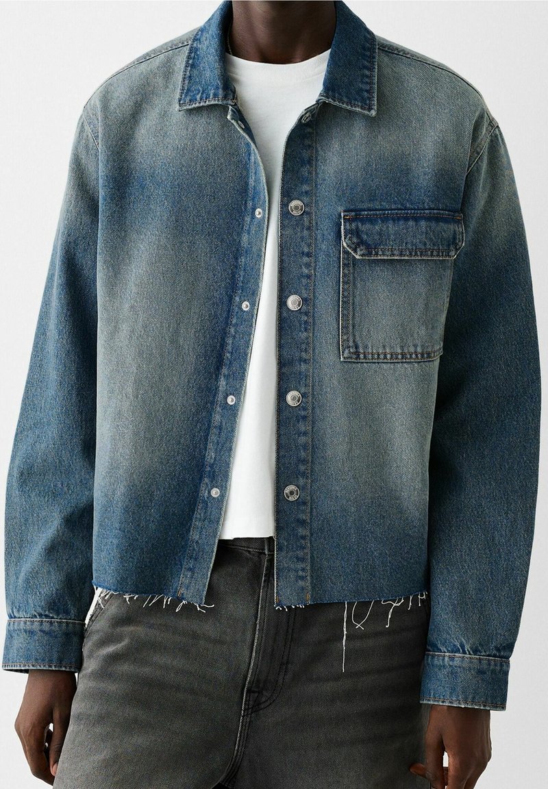 Giacca di jeans in gradiente blu con chiusura a bottone, tasca sul petto e vestibilità ampia. Presenta orlo sfrangiato e maniche a taglio dritto.