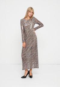 Maxiklær med leopardmønster og lange ermer, laget av et skinnende materiale. Har rund hals og tettsittende silhuett. Båret med svarte hæler.