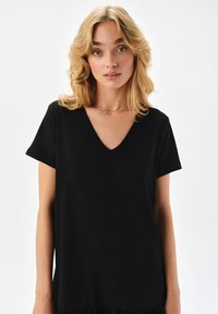 Czarny krótki t-shirt z dekoltem w kształcie V, teksturowany materiał, luźny fason i proste wykończenie, charakteryzujący się prostotą wzornictwa.