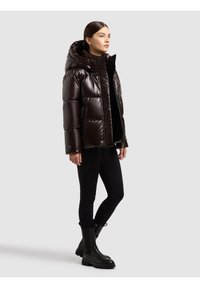 Glansig mörkbrun dunjacka med huva, försedd med dragkedja framtill, quiltad design och avslappnad passform, bärs över svarta leggings och stövlar.