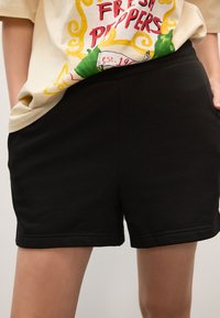 Sorte shorts lavet af blødt stof med elastisk taljebånd og sidelommer, med en ren kant og uden synlige mønstre eller detaljer.