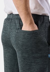 Tummanharmaat, tekstuuriset jogger-housut, joissa on elastinen vyötärö ja vetoketjullinen tasku sivulla. Mukana pieni sininen ja keltainen logo.