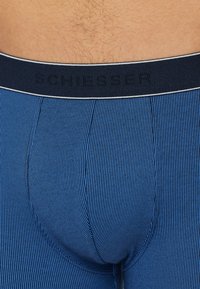 Modré pruhované boxerky s černým pasem sembossovaným logem "SCHIESSER". Materiál vypadá jemně a má přiléhavý střih.
