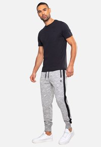Schwarzes Rundhals-T-Shirt kombiniert mit grauen Sweatpants, die vertikale schwarze Streifen und ein Logo-Patch aufweisen, abgerundet mit weißen Sneakers.