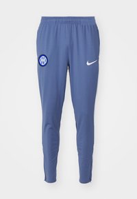 Modré sportovní kalhoty vyrobené z hladké tkaniny s elastickým pasem. Na levém stehně je kulaté logo a bílý znak Nike.