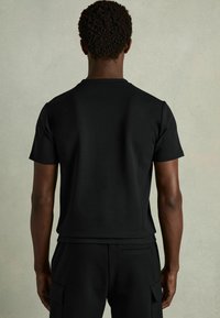 Camiseta negra de manga corta hecha de una suave tela de algodón, con cuello redondo y un diseño ajustado y elegante. Sin gráficos ni patrones.