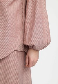 Randig, lättviktig topp i rosa ton med puffärmar och en böjd nederkant. Har fina vita vertikala ränder och en strukturerad yta.