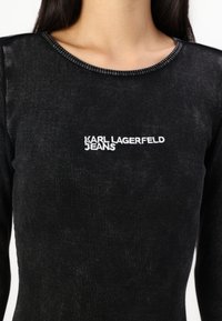 Svart ribbad långärmad topp med rund halsringning, med vit broderad "KARL LAGERFELD JEANS" logotyp på framsidan.