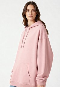 Felpa rosa oversize realizzata in materiale morbido, dotata di tasca a marsupio, polsini a costine e cappuccio con lacci. Texture liscia senza motivi visibili.