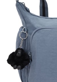 Grå tygryggsäck med en zippered ficka, en mjuk svart gorillanyckelring fäst och strukturerade remmar för grepp.