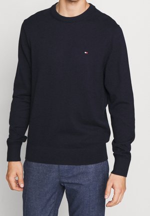 Pull bleu marine, col rond, manches longues, poignets et ourlet côtelés, petit patch logo sur la poitrine, fabriqué dans un tissu doux et texturé.