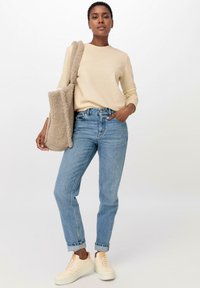 Beige langärmliges Shirt, hellblaue hochtaillierte Jeans, cremefarbene Sneaker und eine tanfarbene flauschige Tote-Tasche. Einfaches und lässiges Outfit.