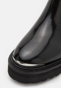 Botte noire brillante avec semelle épaisse et détail en métal argenté sur la partie arrondie de l'orteil.