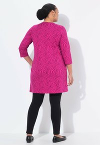 Fuchsia-Tunika mit Zebra-Streifen, 3/4-Ärmeln und geradem Schnitt. Kombiniert mit schwarzen Leggings und flachen Schuhen. Glatte Textur.