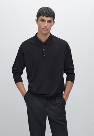 Black pullover with a polo collar, long sleeves, and three-button placket. Smooth texture, relaxed fit, paired with dark trousers.