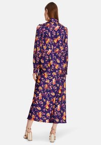 Floral, long-sleeve dress in deep purple fabric with yellow, orange, and pink flowers. Features a flowy, ankle-length design and fitted cuffs.