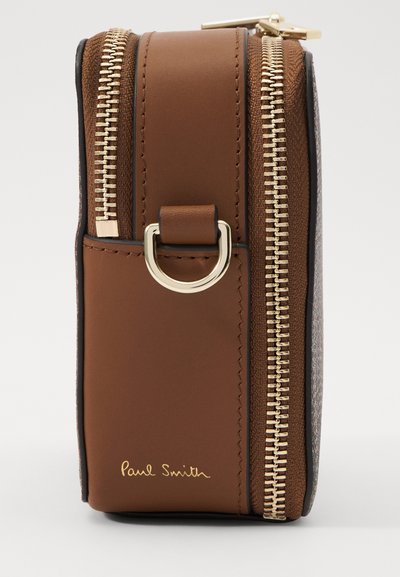 Brūna ādas apvalks ar rāvējslēdzēju un zeltainiem akcentiem, aprīkots ar sānu cilpu un paraksta reljefa uzrakstu. Tekstūrētas detaļas sānos.