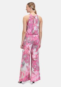 Une combinaison fleurie rose en tissu léger, avec un col halter, un dos nu avec un détail à nouer, et un design à jambes larges.