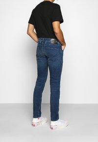 Vaqueros de mezclilla azul de corte ajustado con un lavado oscuro, que presentan una etiqueta de cuero negro en la cinturilla y discretos detalles de costura en los bolsillos traseros.