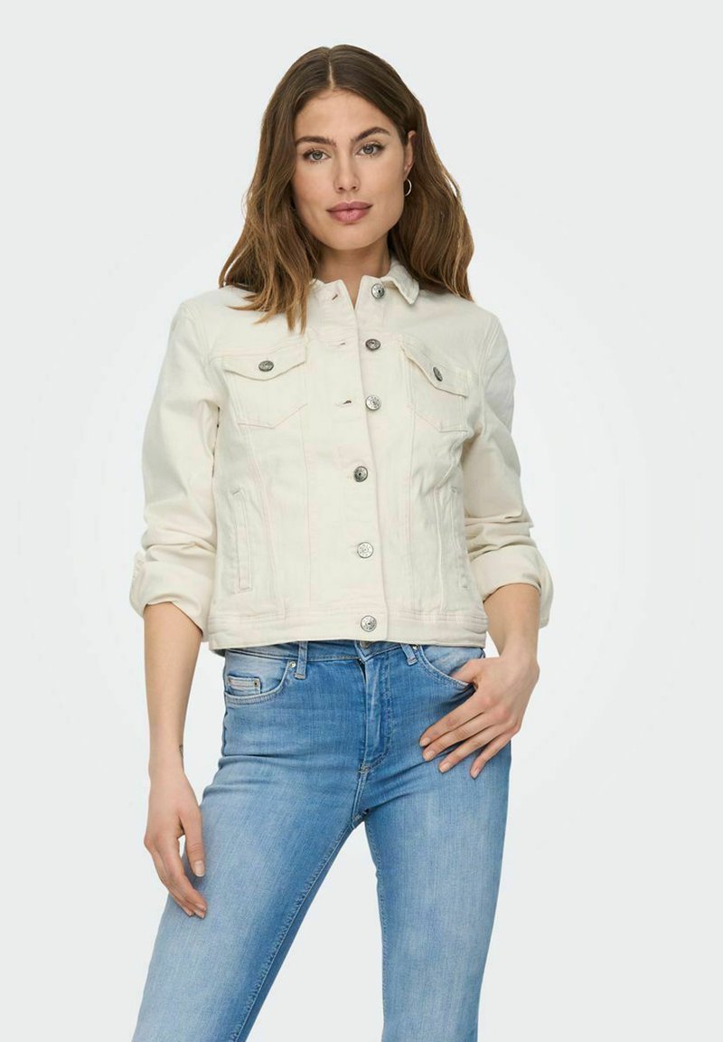 White denim jacket with a classic collar, silver buttons, chest pockets, and rolled sleeves, styled with light blue jeans.