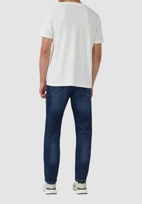 Witte korte mouwen T-shirt, blauwe jeans en witte sneakers met groene accenten. T-shirt heeft een ronde halslijn, jeans hebben een klassieke pasvorm.