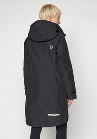 Svart vanntett jakke med hette, som har en reflekterende stripe nederst, justerbare mansjetter og en liten logo på øvre rygg.