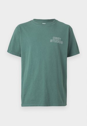 Green cotton t-shirt with a crew neck, short sleeves, and a white "OBEY STUDIOS" logo on the left chest. Soft texture, casual design.