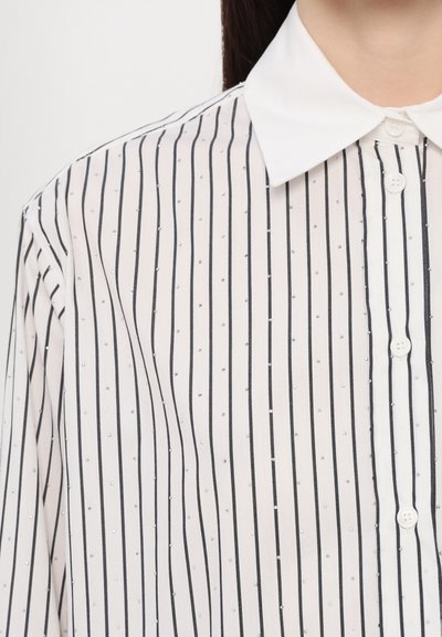 Witte shirt met zwarte verticale strepen en kleine zilveren accenten. Beschikt over een klassieke kraag en knoopsluiting. Gladde textuur.