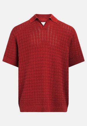 Polo en maille rouge à manches courtes avec motif texturé, col et poignets côtelés, et ouverture en V sans boutons.