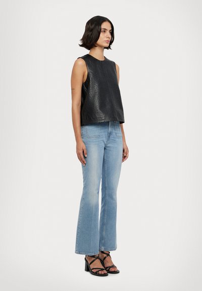 Haut sans manches en cuir noir avec une surface texturée, associé à un jean évasé bleu clair et des sandales à talons noires dotées de fines bretelles.